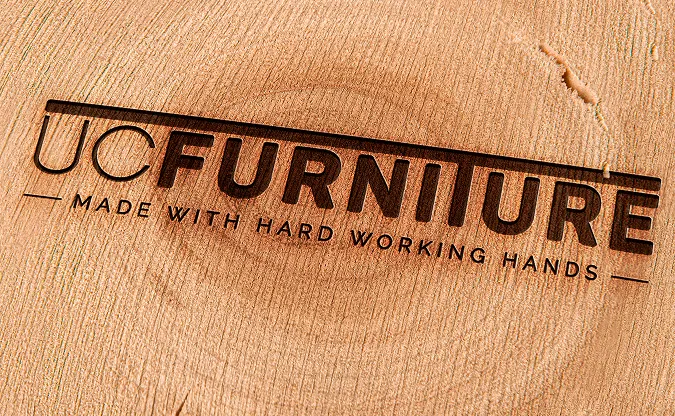 Logo van UCFurniture met de tagline ‘Made with hard working hands’, grafisch gegraveerd op een stuk hout